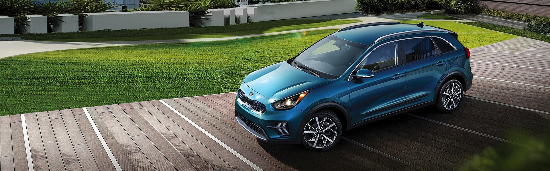 An overhead view of a blue Kia Niro parked on an outdoor wooden deck with grass landscaping.