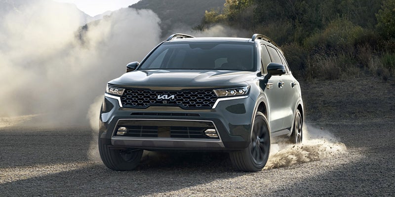Dark gray Kia SUV driving on a gravel road, kicking up dust and dirt in a mountain landscape.