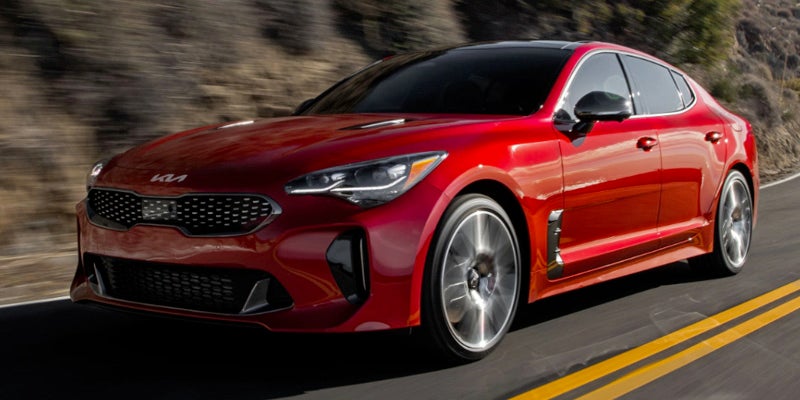 A gleaming red Kia Stinger driving quickly on a mountainous road with motion blur.
