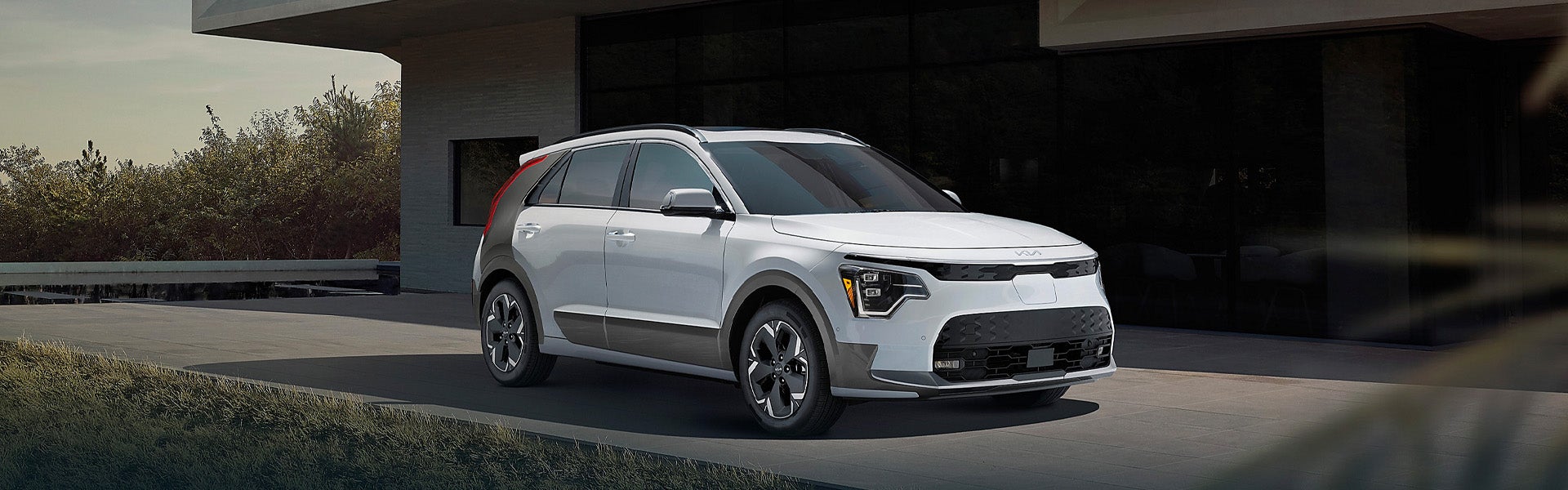 A Kia Niro crossover SUV parked on an asphalt driveway next to a modern building with dark windows.
