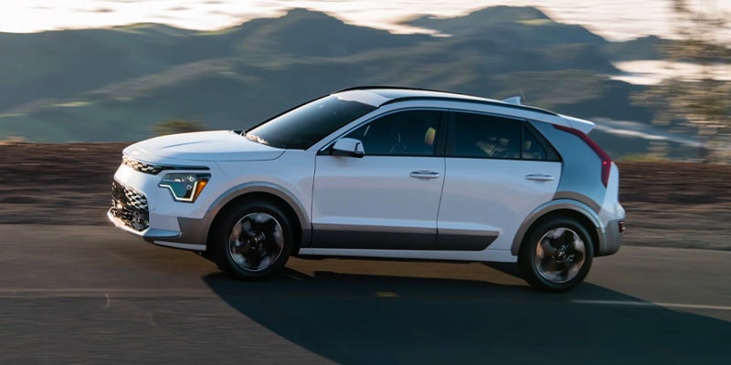 Side view of a Kia Niro EV driving on a road, with mountains and blurred scenery in the background.