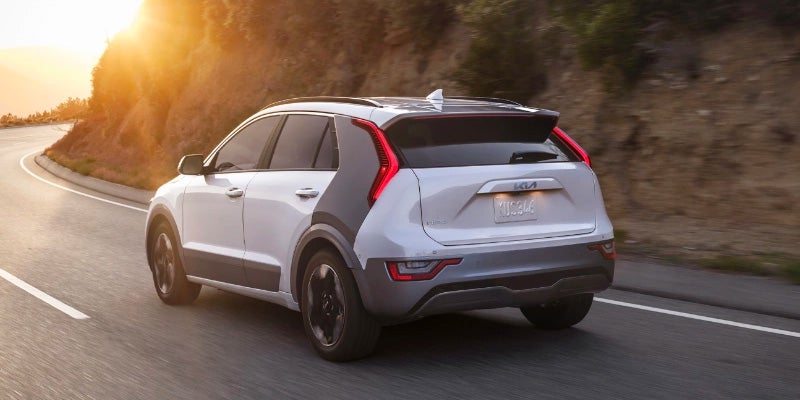 Rear view of a Kia Niro EV driving on a winding road at sunset.