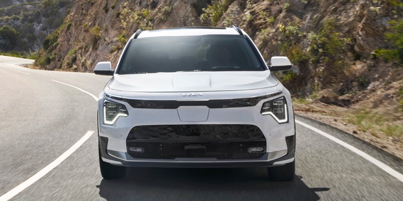 Front view of a Kia Niro EV driving on a winding road with mountains in the background.