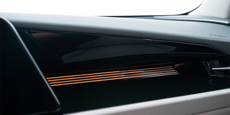 Close-up of a modern car's dashboard with horizontal orange ambient light strips beneath a glossy black panel.