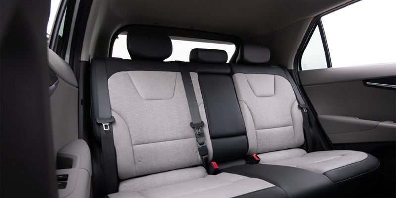 Rear seats of a car with light gray fabric and black leather trim, showing seat belts and headrests.