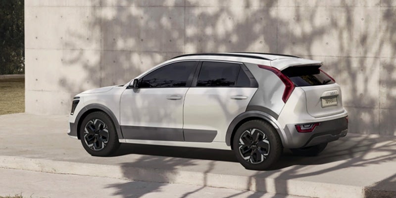 Right side profile of a Kia Niro parked on a concrete slab, casting shadows on the nearby wall.