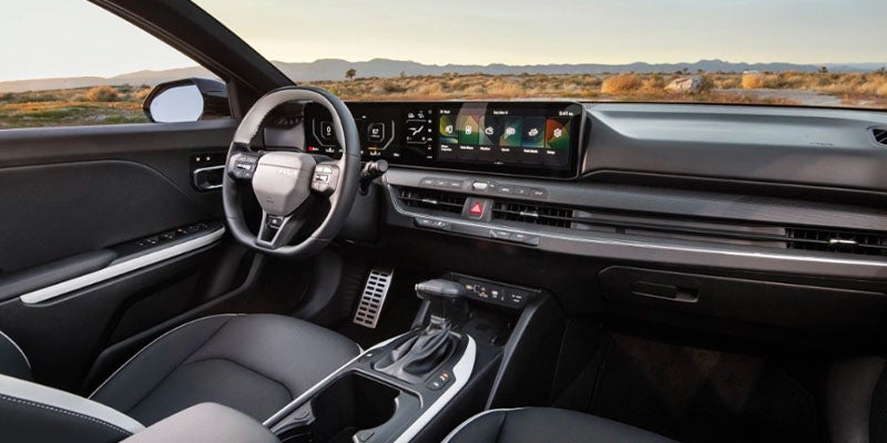 The interior cabin of a modern car with a digital dashboard and touchscreen display, overlooking a desert landscape.