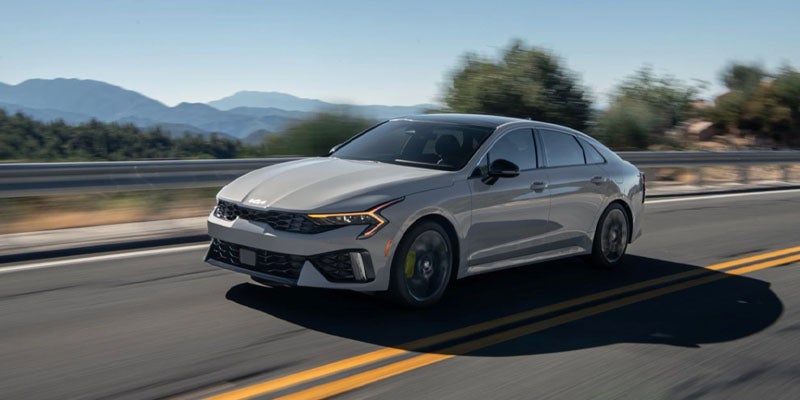 Silver Kia sedan driving on an open road with mountains behind