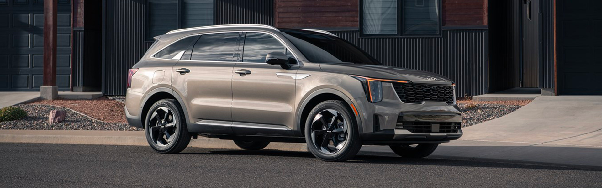 Champagne-colored Kia SUV parked on a paved street in front of a modern home with black siding.