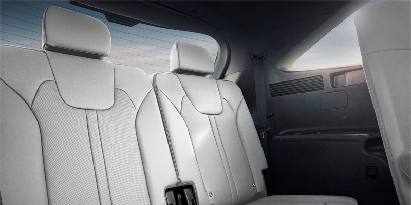 White perforated car seats in the second row of a vehicle with the back window visible.