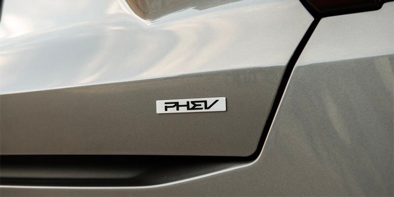 A silver PHEV badge on the light brown rear of a car.