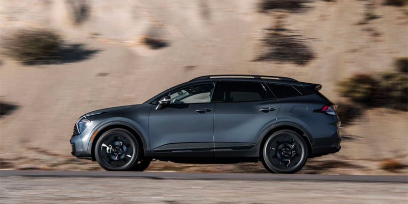 Side profile of a dark grey SUV driving quickly on a road, with a blurry desert landscape in the background.