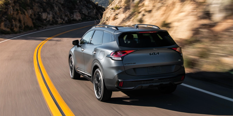 Rear view of a gray Kia Sportage Plug-In Hybrid driving on a curving mountain road
