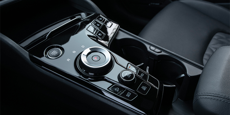 Modern car interior showing the shiny black center console with a rotary shifter, buttons, and cupholders.
