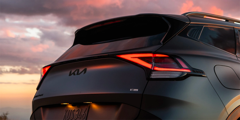 Rear view of a dark gray Kia SUV with red LED taillights against a dramatic sunset sky.