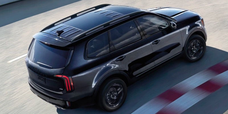 Overhead shot of a glossy black Kia Sorento SUV with a panoramic sunroof and roof rack on a parking garage rooftop.