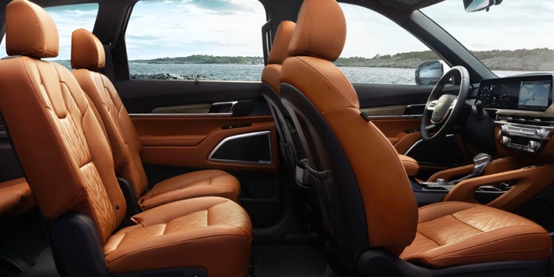 The interior of a vehicle with two rows of tan leather seats and a dashboard with screens, viewed from the back.