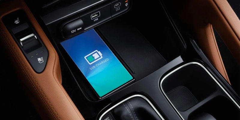A phone wirelessly charging to 50% in the center console of a car, with brown leather trim visible.