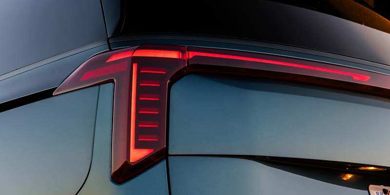 A sleek, dark vehicle's rear features a distinctive red taillight design with vertical and horizontal elements.