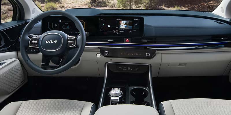 View inside a car dashboard, showcasing a large infotainment touchscreen and a steering wheel with the Kia logo.