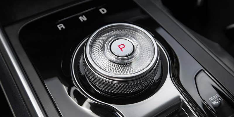 A close-up of a central car gear selector knob with a red 'P' park button and 'R N D' gears.