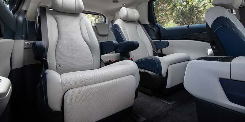 Interior view of a vehicle showing two rows of light gray and dark blue captain's seats with full armrests.