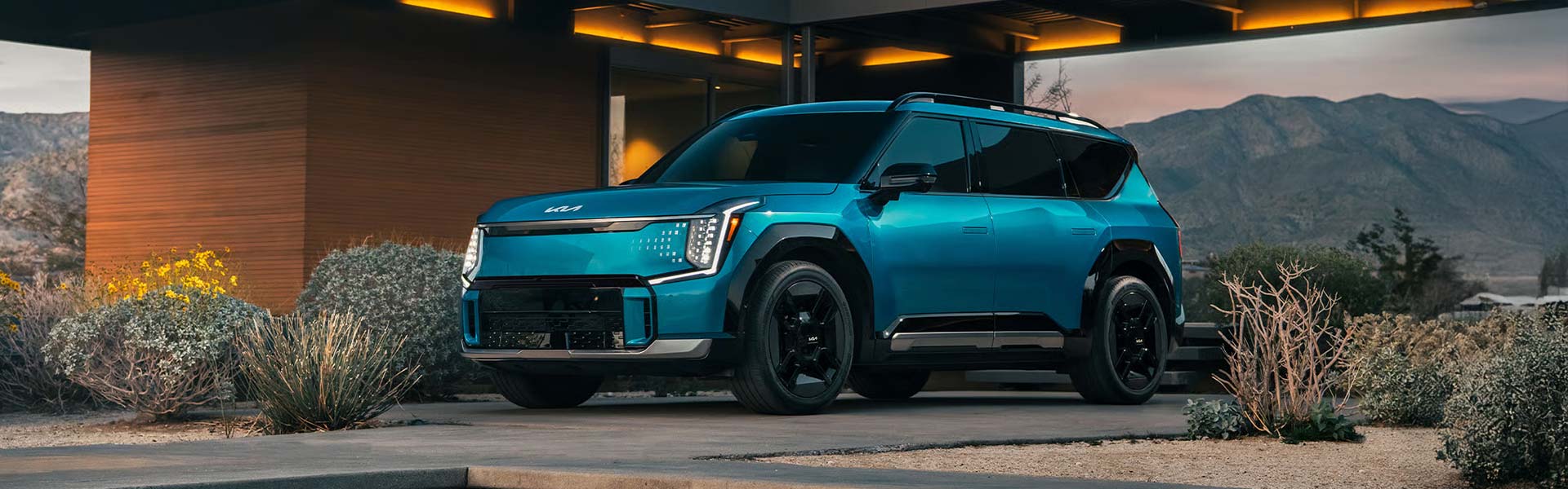 Kia EV9 electric SUV sits parked under a covered entryway with mountains in the background.