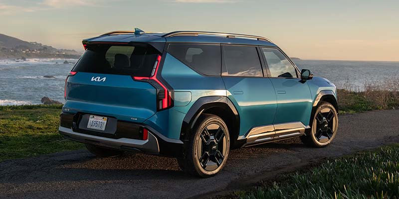 Kia EV9 SUV sits parked with the ocean and coastline visible behind it.