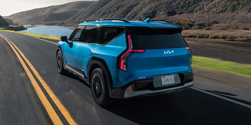 Kia EV9 drives along a winding coastal road with mountains in the background.