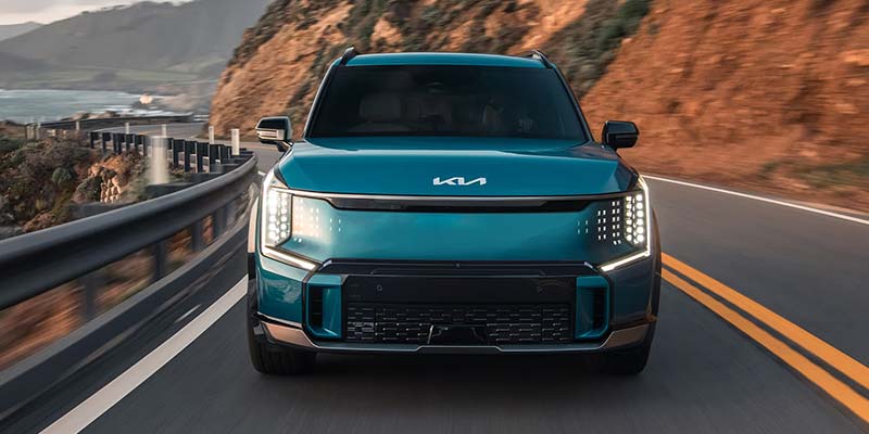 Kia EV9 drives down a coastal highway with blurred scenery.