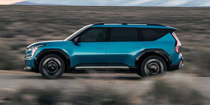 Kia EV9 SUV drives along a desert road, kicking up dust.