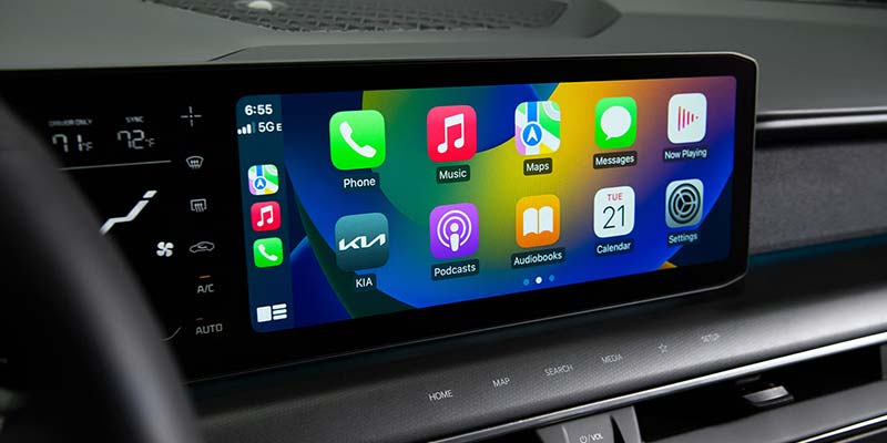 A car's infotainment screen displays various app icons, including Apple Music and Maps.