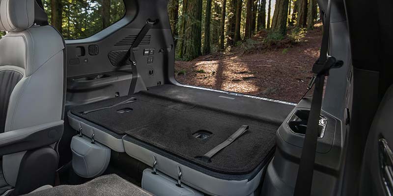 An SUV's spacious interior shows a flat cargo area with seats folded down, revealing a forest backdrop.