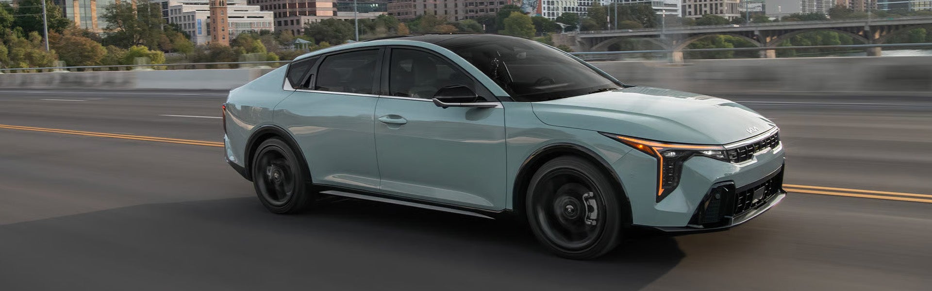 Kia K4 sedan driving on city highway with skyline background
