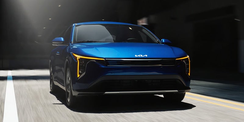 Kia K4 sedan front view driving through urban street