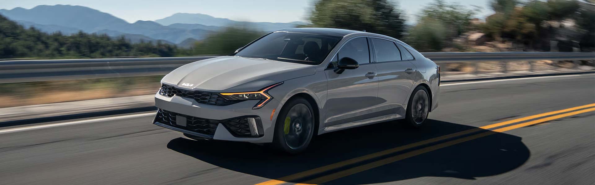 Kia sedan driving on highway with mountain background