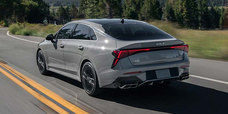 Rear view of Kia K5 sedan driving on forest road