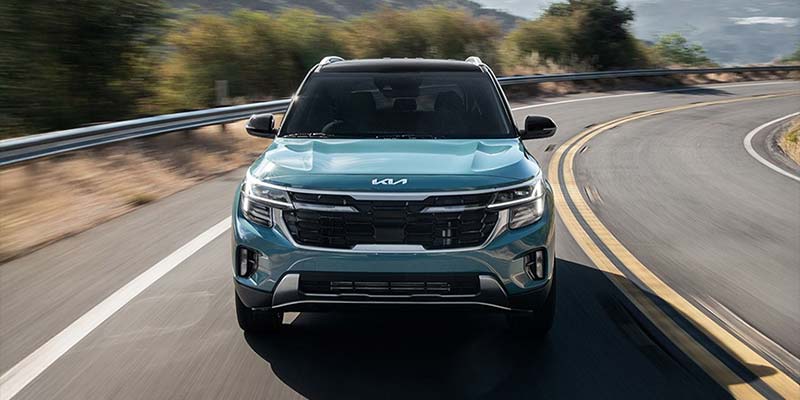 Kia Seltos SUV driving on a winding road with motion blur, viewed from the front.