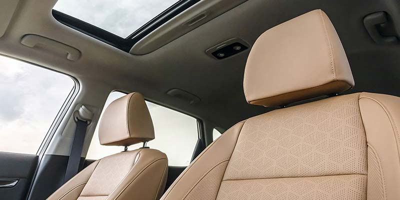 Interior of a car showing two rows of beige leather seats under an open sunroof.