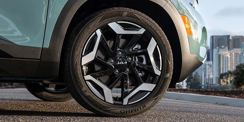 Close-up of a car's front wheel with a dynamic black and silver rim, parked on asphalt.