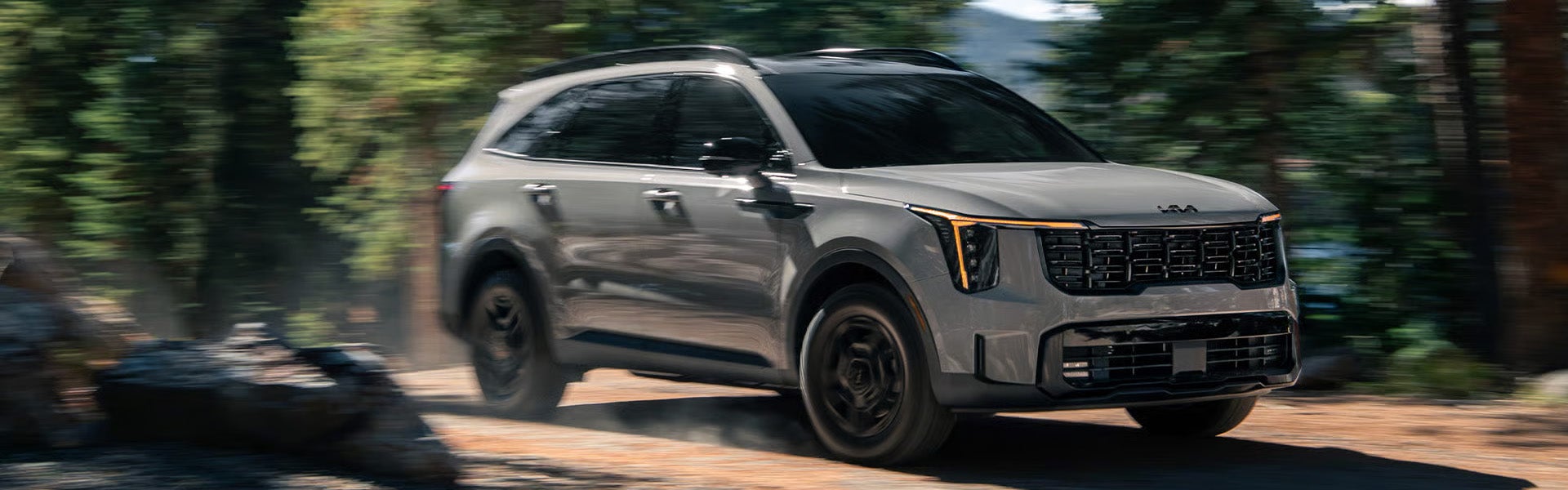 SUV with black wheels driving fast on a dirt road, trees blurred in the background.