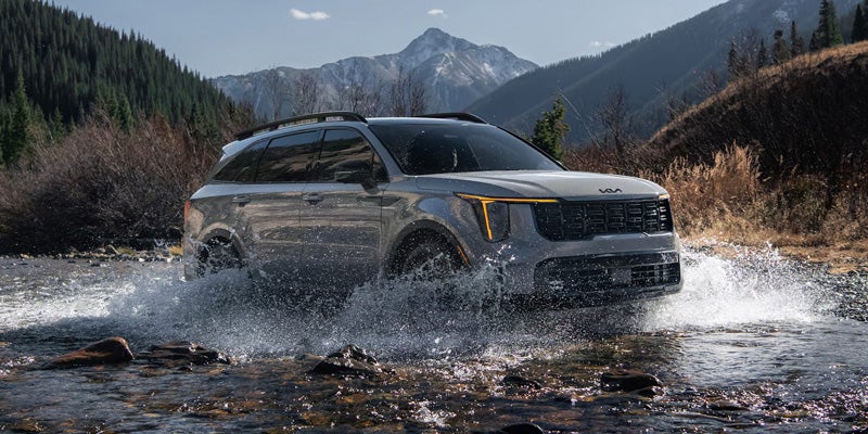 Kia Sorento SUV drives through a shallow river in a mountain valley.