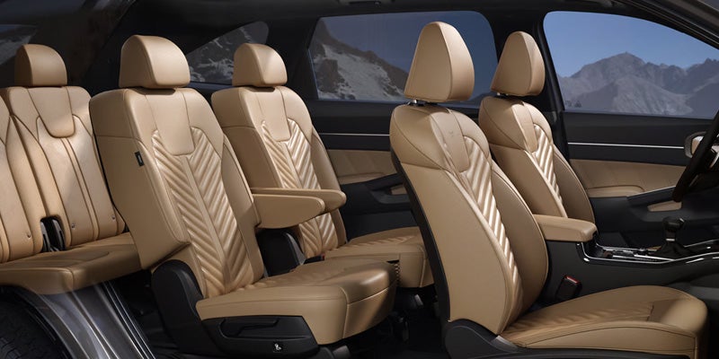 Four rows of luxurious tan leather car seats with patterned stitching, viewed from the front passenger side.