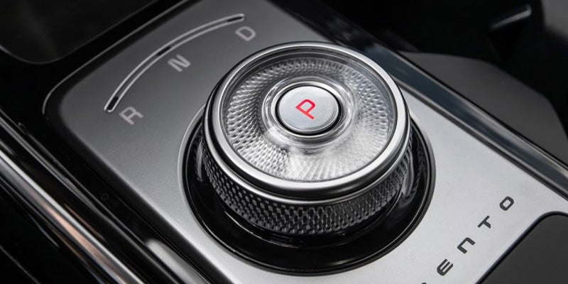 A modern metallic car gear selector dial with a red "P" for Park in the center, next to "R, N, D".