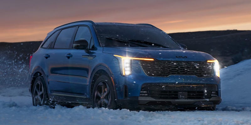 KIA Sorento SUV driving through snow at dusk, with its headlights on.
