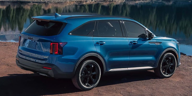 Rear view of a Kia Sorento SUV with black wheels, parked on dirt next to a body of water.