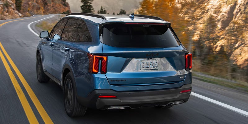Rear view of a Kia Sorento driving on a winding mountain road with autumn foliage.