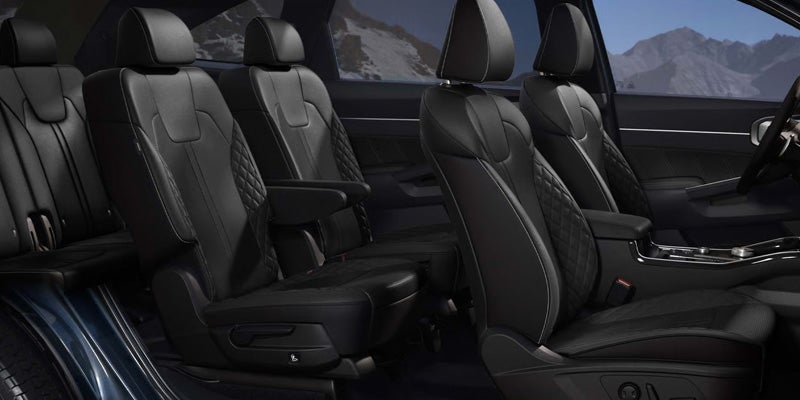 Interior of a car with three rows of black leather seats, some featuring diamond-stitched patterns.