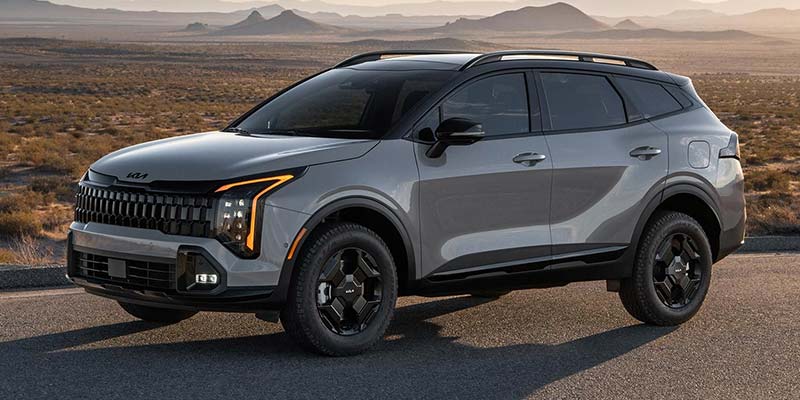 A gray Kia Sportage SUV on a paved road with a desert and mountains in the background.