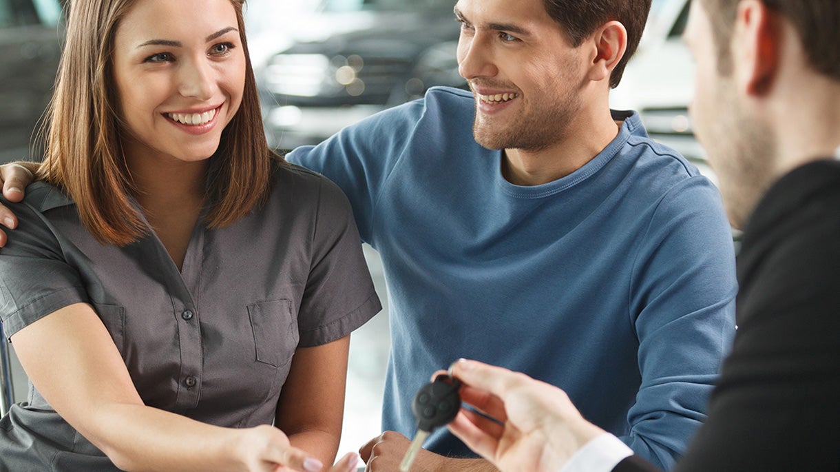 A beaming couple happily accepts car keys from a salesperson.